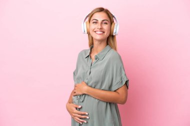 Genç Uruguaylı kadın mavi arka planda izole edilmiş hamile ve müzik dinliyor.