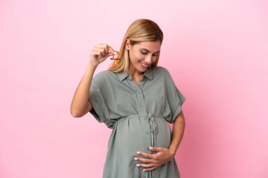 Genç Uruguaylı kadın mavi arka planda izole edilmiş hamile ve emzik taşıyor.