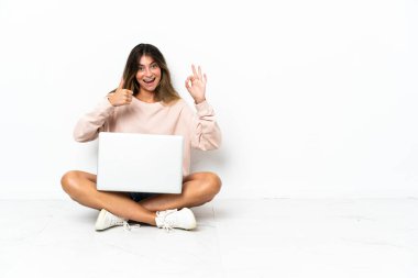 Yerde dizüstü bilgisayarı olan genç bir kadın beyaz arka planda izole bir şekilde oturuyor.