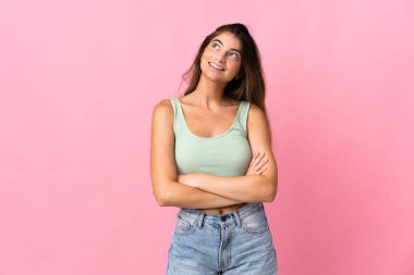 Genç beyaz kadın pembe arka planda izole edilmiş gülümserken yukarı bakıyor.