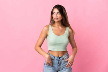 Pembe arka planda soyutlanmış genç beyaz kadın yana bakıyor ve gülümsüyor.