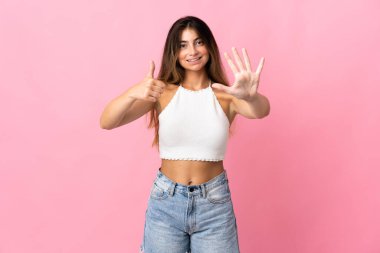 Pembe arka planda izole edilmiş genç beyaz kadın parmaklarıyla altısını sayıyor.