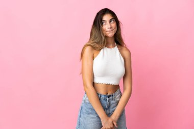 Pembe arka planda izole edilmiş genç beyaz kadın yukarı bakarken şüpheleri var.