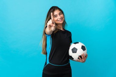 Genç futbolcu kadın mavi arka planda izole edilmiş ve parmağını kaldırıyor.