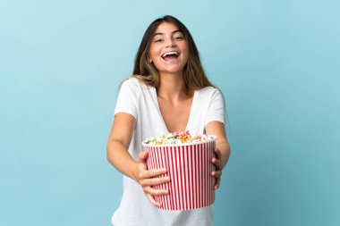 Mavi arka planda izole edilmiş beyaz bir kadın elinde koca bir kova patlamış mısır tutuyor.