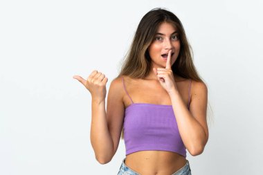 Beyaz arka planda izole edilmiş genç beyaz bir kadın yan tarafı işaret ediyor ve sessiz hareketler yapıyor.