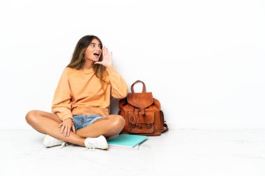 Genç bir kız öğrenci dizüstü bilgisayarla yerde oturuyor beyaz arka planda izole edilmiş ağzı sonuna kadar açık bağırıyor.