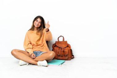 Yerde dizüstü bilgisayarlı genç bir bayan oturuyor. Beyaz arka planda izole edilmiş. Para hareketi yapıyor.