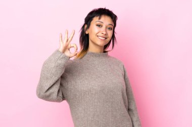 Genç Uruguaylı kadın izole edilmiş pembe arka planda parmaklarıyla tamam işareti gösteriyor.
