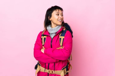 Genç dağcı kız büyük bir sırt çantasıyla soyutlanmış pembe arka planda gülüyor.