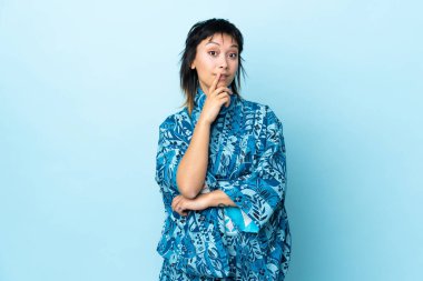 Kimono giyen genç bir kadın soyutlanmış mavi arka planda kuşkuları var.