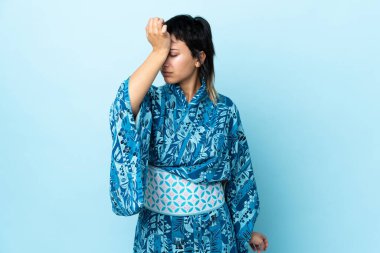 Kimono giyen genç bir kadın soyutlanmış mavi arka plan ve baş ağrısı.