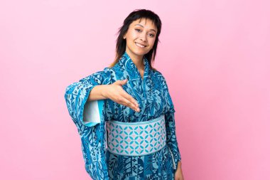 Kimono giyen genç bir kadın izole edilmiş mavi arka planda iyi bir anlaşma için el sıkışıyor.