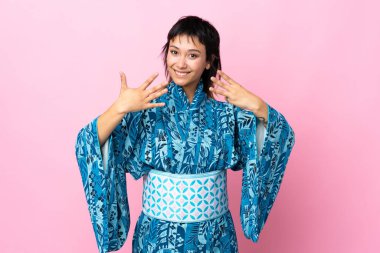 İzole edilmiş mavi arka planda kimono giyen genç bir kadın sekiz parmaklı sayıyor.