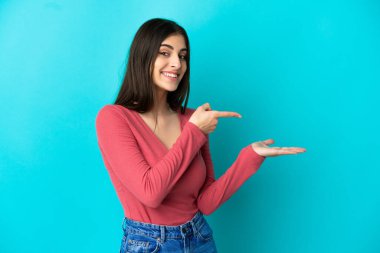 Mavi arka planda izole edilmiş genç beyaz kadın bir ilan vermek için avucunun içinde hayali bir fotokopi makinesi tutuyor.