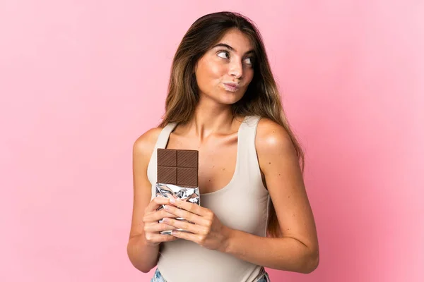 Mladá Běloška Žena Izolované Růžovém Pozadí Čokoládovou Tabletu Mají Pochybnosti — Stock fotografie