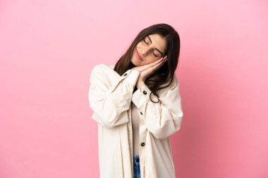 Pembe arka planda izole edilmiş genç beyaz bir kadın uyku jesti yapıyor.