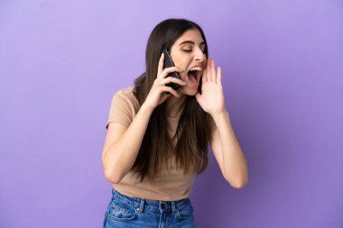Mor arka planda izole edilmiş cep telefonu kullanan beyaz bir kadın ağzı sonuna kadar açık bağırıyor.