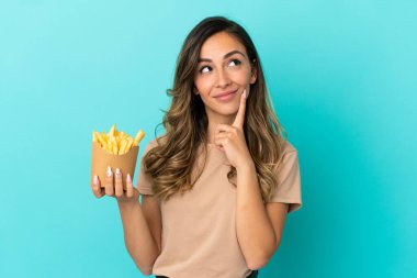 Kızarmış cipsleri izole edilmiş arka planda tutan genç bir kadın, yukarı bakarken bir fikir düşünüyor.