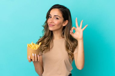 Kızarmış cipsleri izole edilmiş arka planda tutan genç bir kadın parmaklarıyla tamam işareti gösteriyor.
