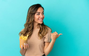 Kızarmış cipsleri izole edilmiş arka planda tutan genç bir kadın bir ürünü sunmak için kenarı işaret ediyor.