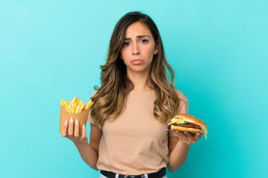 Arkaplanda kızarmış cips ve hamburger tutan genç bir kadın.