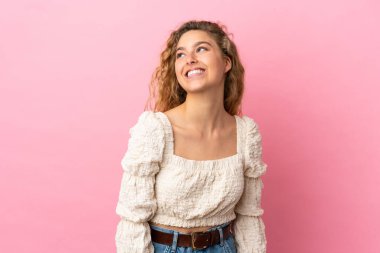 Pembe arka planda izole edilmiş genç sarışın kadın yukarı bakarken bir fikir düşünüyor.