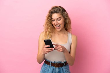 Pembe arka planda izole edilmiş genç sarışın kadın cep telefonuyla mesaj ya da e-posta gönderiyor.
