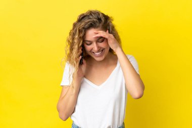 Sarı arka planda izole edilmiş cep telefonu kullanan genç sarışın kadın gülüyor.