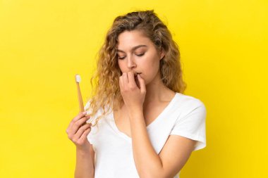 Sarı arka planda dişlerini fırçalayan beyaz bir kadın şüpheleri var.