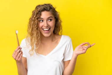 Sarı arka planda dişlerini fırçalayan beyaz bir kadın çözümü bulmak için parmağını kaldırıyor.