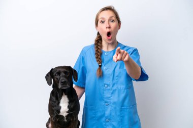 Beyaz arka planda izole edilmiş köpekli genç veteriner kadın şaşırmış ve ön tarafı işaret ediyor.