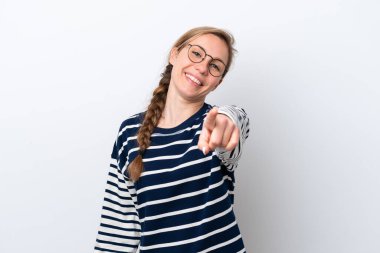 Beyaz arka planda izole genç beyaz kadın mutlu bir ifadeyle ön tarafı işaret ediyor.