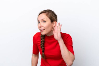 Beyaz arka planda izole edilmiş genç beyaz kadın elini kulağına koyarak bir şeyler dinliyor.