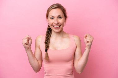 Pembe arka planda izole edilmiş genç beyaz kadın galibiyeti kutluyor.