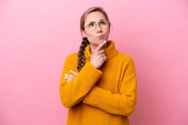 Pembe arka planda izole edilmiş genç beyaz kadın yukarı bakarken şüpheleri var.