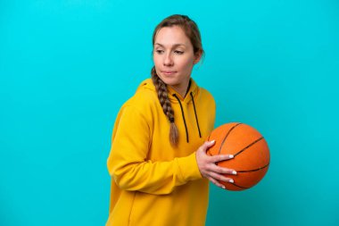 Genç beyaz kadın mavi arka planda izole edilmiş basketbol oynuyor.