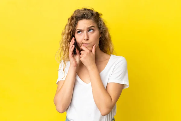 Молодая Блондинка Помощью Мобильного Телефона Изолированы Желтом Фоне Сомнениями — стоковое фото