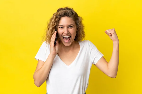 Młoda Blondynka Pomocą Telefonu Komórkowego Odizolowany Żółtym Tle Robi Silny — Zdjęcie stockowe