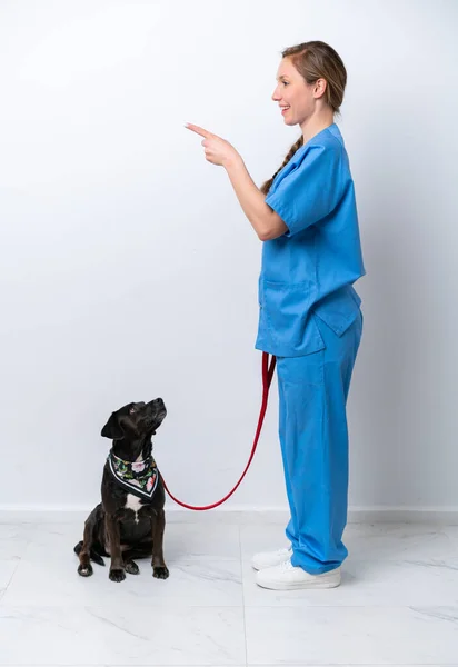 Full body veterinarian woman with a dog isolated on white background pointing to the side to present a product