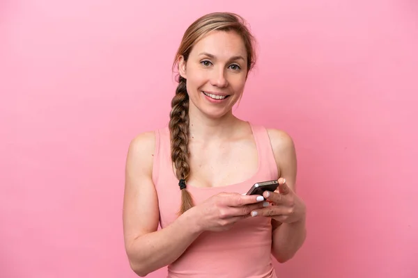 ピンクの背景に孤立した若い白人女性が携帯電話でメッセージを送る — ストック写真