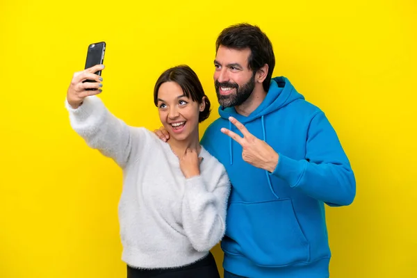 年轻的高加索夫妇在黄色背景上被隔离 用手机自拍 — 图库照片