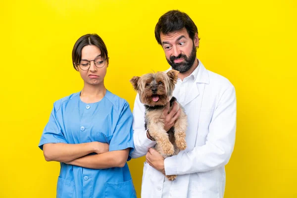 Young veterinarian couple with dog isolated on yellow background with sad expression