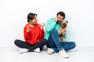 Beyaz arka planda izole edilmiş evcil hayvanlarıyla yerde oturan beyaz bir çift hayal kırıklığına uğramış ve bağırıyor.