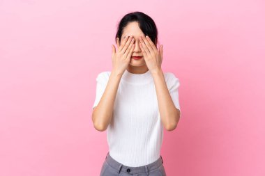 Pembe arka planda izole edilmiş genç Vietnamlı kadın gözlerini elleriyle kapatıyor.
