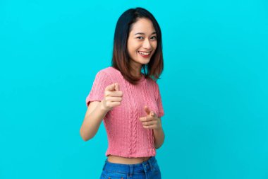 Genç Vietnamlı kadın mavi arka planda izole edilmiş şaşırmış ve ön tarafı işaret ediyor.