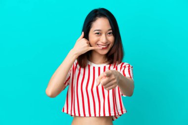 Genç Vietnamlı bir kadın mavi arka planda izole edilmiş telefon hareketlerinde bulunuyor.