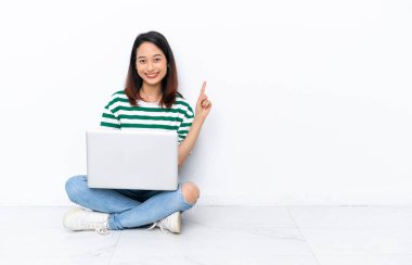 Diz üstü bilgisayarı olan genç Vietnamlı kadın beyaz duvarda izole bir şekilde oturuyor.