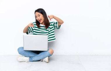 Yerde dizüstü bilgisayarı olan genç Vietnamlı bir kadın beyaz duvarda izole bir şekilde oturuyor.