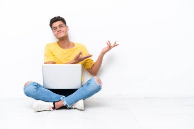 Genç adam beyaz arka planda izole bir şekilde yerde oturuyor. Davet edilmek için ellerini yana uzatıyor.